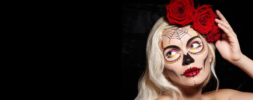 Beautiful Halloween Make-Up Style. Blond Model Wear Sugar Skull Makeup with Red Roses, pale Skin Tones and Waves Hair. Dia de los Muertos or Santa Muerte concept. Copy Space