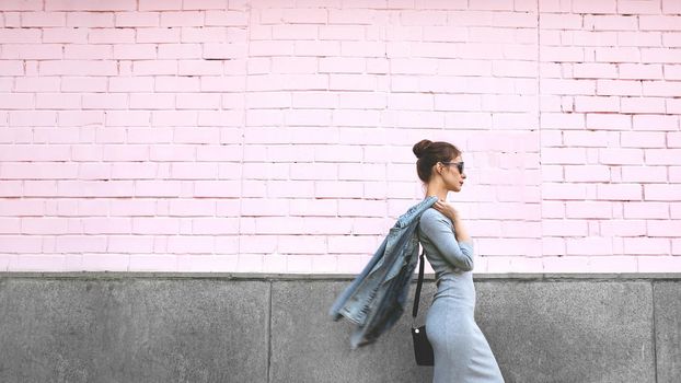 Street Style Shoot of Woman on Pink Wall. Swag Girl Wearing Jeans Jacket, grey Dress, Sunglass. Fashion Lifestyle Outdoor