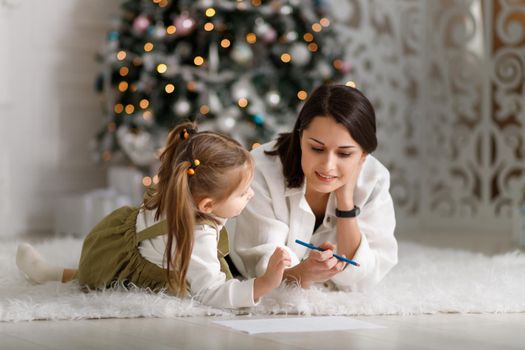 Cute little girl with her mother is writing a letter to santa claus in christmas interior.