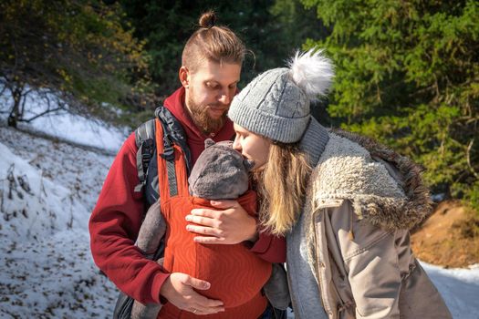 Young family with their baby in ergonomic baby carrier in winter outdoor adventure.