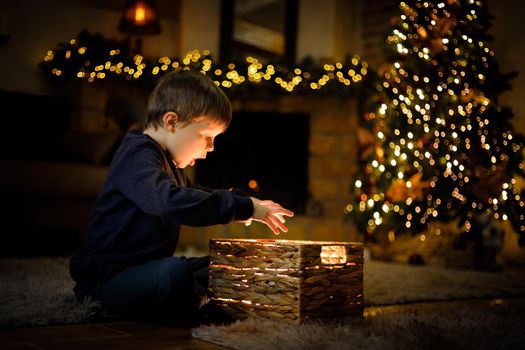 Boy 5-7 y.o. opened a miracle New Year's gift in a Christmas interior with a Christmas tree and garlands. Selective soft focus, film grain effect