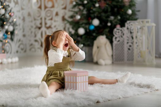 Enthusiastic surprised delight emotional cute girl with new year gift while sitting with closed eyes in christmas interior.