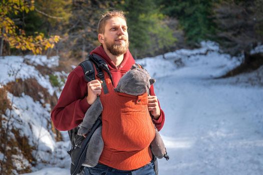 Young father with his baby boy in ergonomic baby carrier in winter forest.