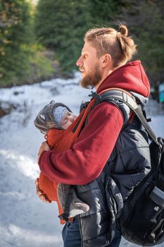 Young bearded babywearing father with his baby in sling winter walking outdoor