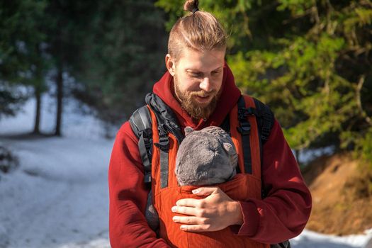 Young bearded father with his baby boy in ergonomic baby carrier in winter outdoor.