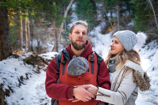 Portrait of young babywearing family with his son in baby sling, winter weekend outdoor.