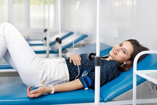 Young beautiful smiling woman patient on medical couch get medical drip procedure.