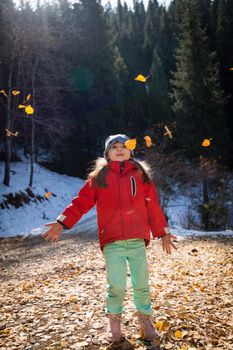 Happy smiling little girl playing with golden autumn leaves in winter sunny day.