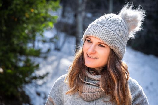 Winter portrait of blond young woman in grey sweater and beanie hat outdoor.