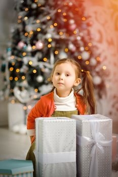 Cute little girl with a Christmas gift by a Christmas tree in cozy living room.