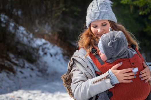 Young mother with her baby in ergonomic baby carrier in winter hiking. Babywearing and active mother concept.