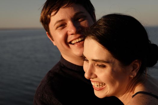 Close-up portrait of a laughing couple in love on the background of the sea in the sunset lighting.