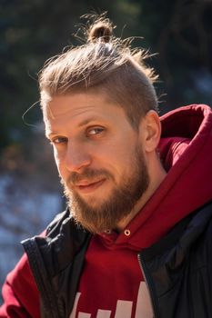 Outdoor vertical portrait of blond bearded smiling hipster man in nature.