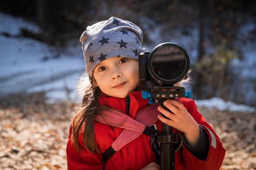 Portrait of happy little girl with camera in star hat outdoors.
