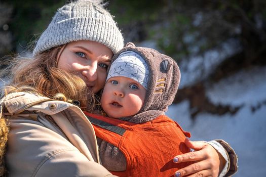 Young caucasian blond mother with his baby boy in ergonomic baby carrier in winter outdoor.