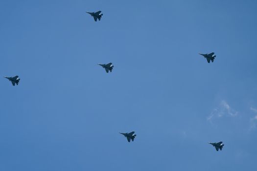 Victory parade of army air force over the city. Group of military aircraft shows aerobatics in blue sky against background of clouds. Representation of aviation equipment.