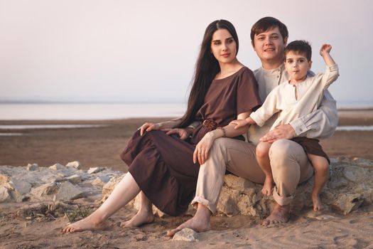 Portrait of caucasian family of three posing on beach. Family look linen clothes.
