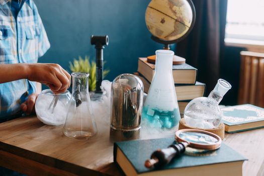 Children's hands are doing a chemical experiment. Flasks with solutions and chemical formulas on the blackboard, books and a globe in the school classroom. Back to school. School and preschool education.