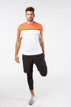 Attractive football player warm-up muscles before match. Serious-looking determined sportsman in activewear, stretch foot behind, look assertive camera, prepare body for run, jogging training session.