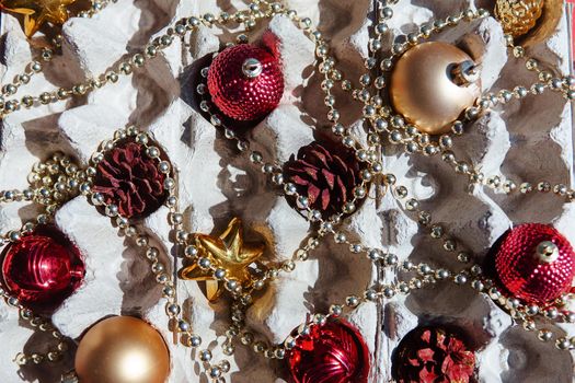 Christmas tree toys in the egg tray on a red background. Top view. The concept of New Year's holidays and Christmas. Red and gold colors.