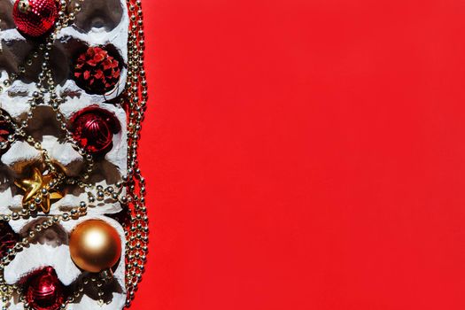 Christmas tree toys in the egg tray on a red background. Top view. The concept of New Year's holidays and Christmas. Red and gold colors.