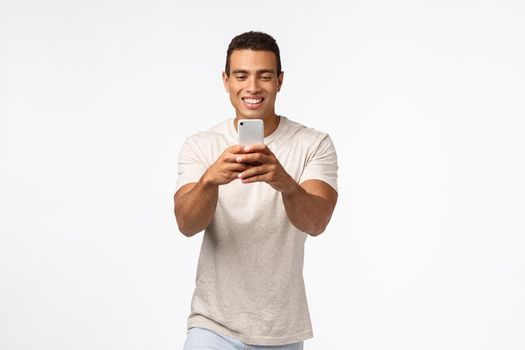 Cheerful, excited good-looking brazilian man with strong muscles, holding smartphone, looking enthusiastic gadget screen, record video, attend amusing event, taking photos on telephone camera.