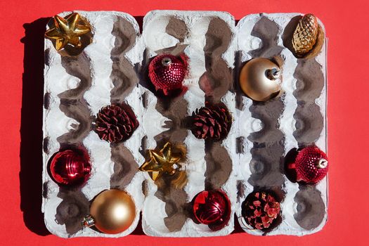 Christmas tree toys in the egg tray on a red background. Top view. The concept of New Year's holidays and Christmas. Red and gold colors.