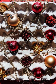 Christmas tree toys in the egg tray on a red background. Top view. The concept of New Year's holidays and Christmas. Red and gold colors.