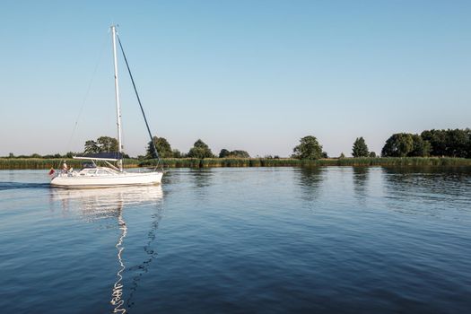 A white yacht with lowered sails sails in the lagoon. Quiet evening, well visible reflection of the ship's mast in the water. Horizontal photo