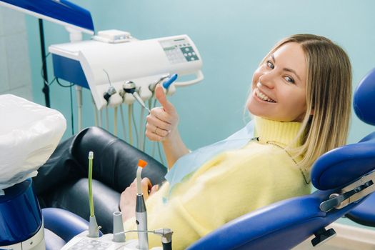 Beautiful girl patient shows the class with her hand while sitting in the Dentist's chair.