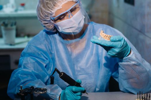 A dental technician in protective clothing is working on a prosthetic tooth in his laboratory.