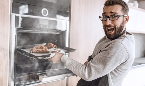 close up. a young man takes out of the oven tray of croissants. photo with copy space