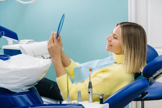 The girl smiles and looks in the mirror in dentistry.