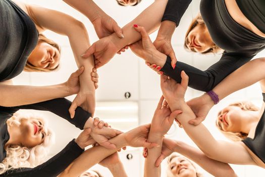 Team of people holding hands. Group of happy young women holding hands. Bottom view, low angle shot of human hands. Friendship and unity concept.