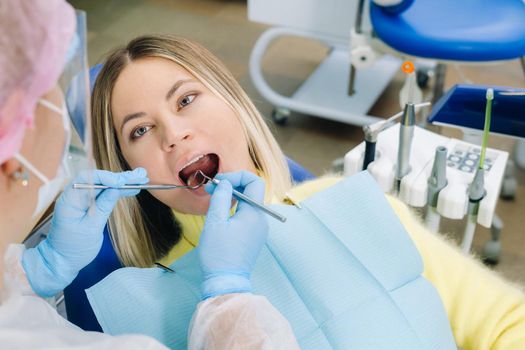 a dentist in a protective mask sits next to him and treats a patient in the dental office.