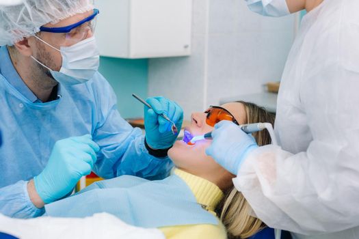 A male dentist with dental tools drills the teeth of a patient with an assistant. The concept of medicine, dentistry and healthcare.