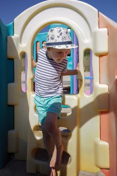 A little boy in a striped shirt performs workout exercises on a colourful beach playground