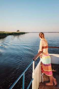A beautiful young girl stands at the front of the ship and watches the quiet evening sunset