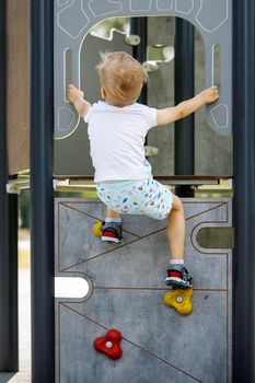 A young mountaineer trains to climb the climbing wall. Active child time spending concept image.