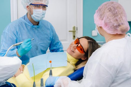 The patient smiles in the dentist's chair in a protective mask and instrument before treatment in the dental office.