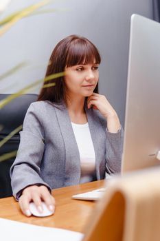 A brunette woman at a computer in the workplace. Business concept.