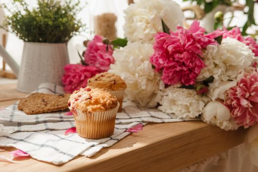 The kitchen countertop is decorated with peonies. The interior is decorated with spring flowers. Pink peonies and sweet cupcakes on a wooden countertop. Interior details