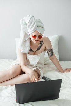 Tver, Russia-august 2, 2021 A woman after a shower is lying on the couch with a laptop and an eye mask at the same time. The concept of multitasking in the twenty-first century.