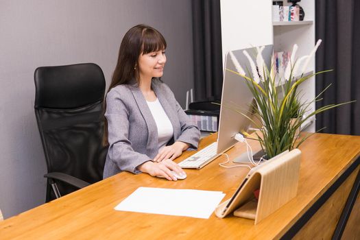 A brunette woman at a computer in the workplace. Business concept.