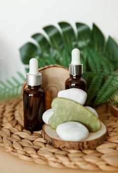 Jade Gua sha scraper and bottles of cosmetic serum for the face on wooden stands. Concept zero waste.