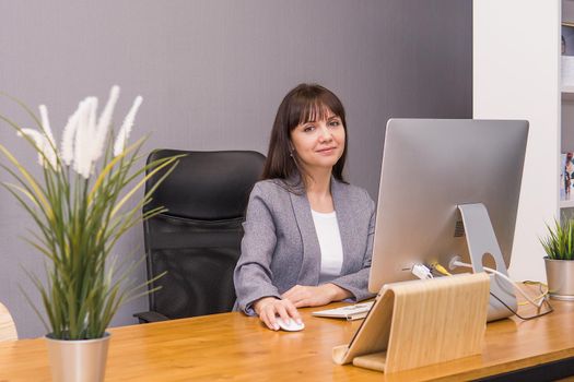 A brunette woman at a computer in the workplace. Business concept.