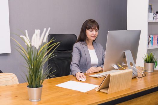 A brunette woman at a computer in the workplace. Business concept.