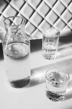 Water in glasses and in a vase on white steel. Shadows hard light. Minimalism