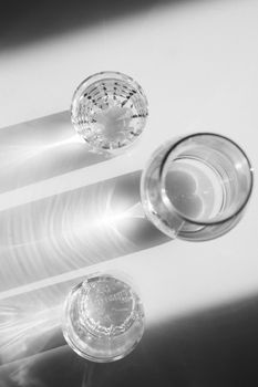Water in glasses and in a vase on white steel. Shadows hard light. Minimalism
