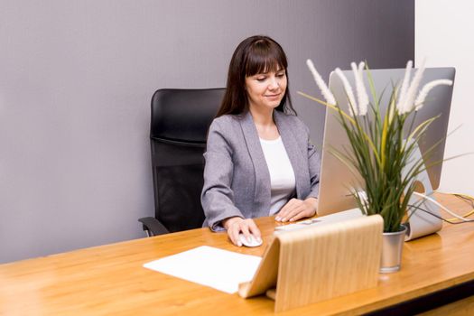 A brunette woman at a computer in the workplace. Business concept.